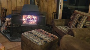 Un accogliente soggiorno con stufa a legna, pareti in legno, un divano e un pouf decorato.