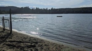 Una spiaggia con un molo di legno che si protende in acque calme, circondata da colline boscose.