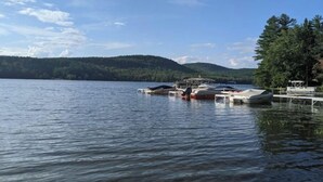 Un lago tranquillo con barche ormeggiate a un molo, circondato da colline ricoperte di boschi.