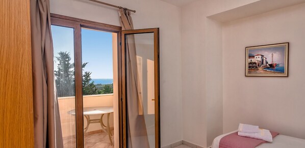 A room with a balcony, a bed with a red blanket, and a painting on the wall.