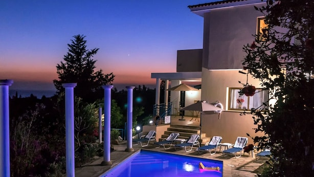 Un espace aménagé au bord de la piscine, avec des chaises longues, une piscine et une vue sur la mer au crépuscule.