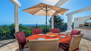 Une terrasse extérieure avec une table ronde, des chaises en osier et un grand parasol.