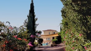 Une maison avec un toit en tuiles, entourée d’une végétation luxuriante et de plantes en fleurs.