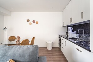A compact living space with a kitchenette, a dining area, and a small trash bin. - Savory Orange Apartment, WiFi, AC !New! (Lisboa)