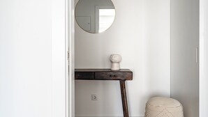 Una habitación con un espejo redondo, una mesita con un objeto decorativo y una pared lisa.