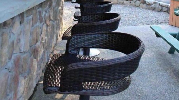 A covered outdoor seating area with wicker chairs and a stone wall.
