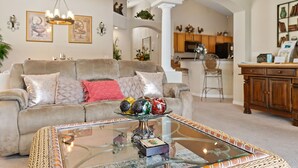 A living room with a glass coffee table, beige sofa, and decorative items. - 4BR/3Bath Home, pool/spa, game room, lake view. Closer to ALL ATTRACTIONS (Kissimmee)