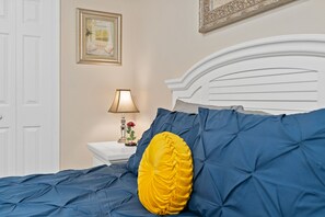 A bedroom with a white headboard, a blue bedspread, and a yellow pillow.