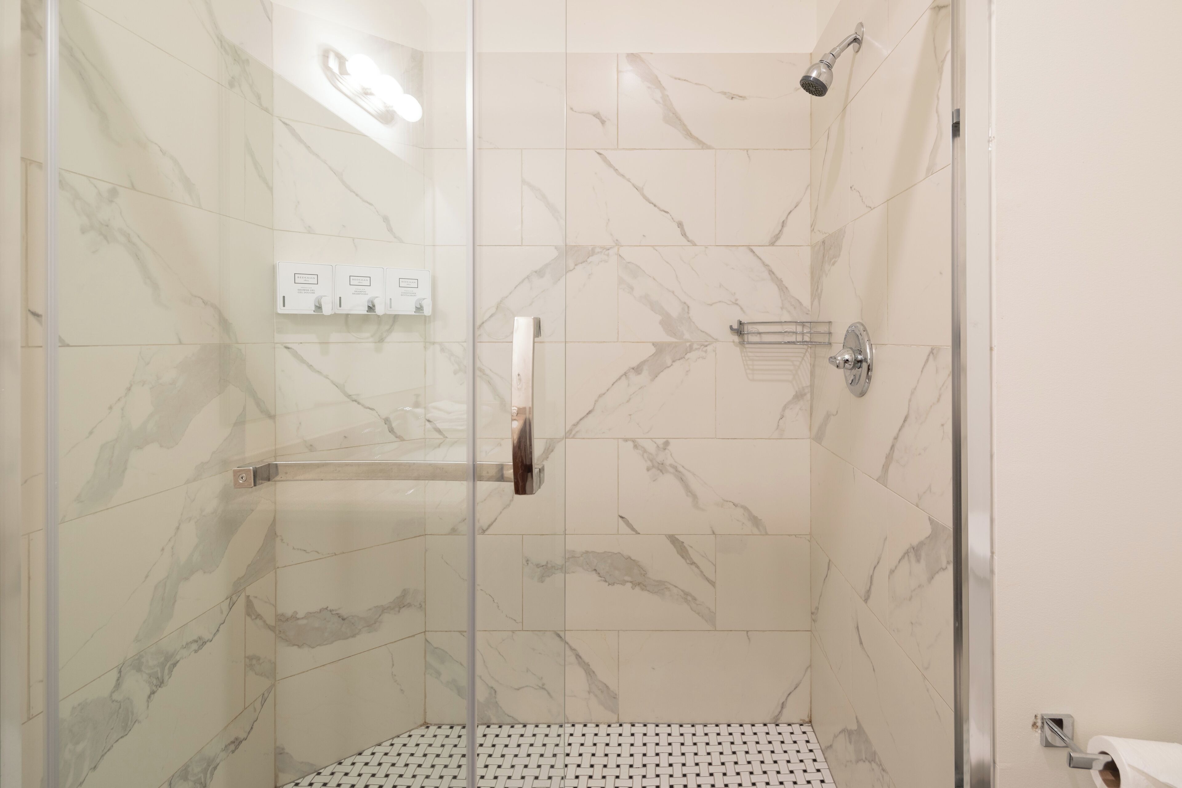 A glass-enclosed shower with marble tiles, a handrail, and a control panel.