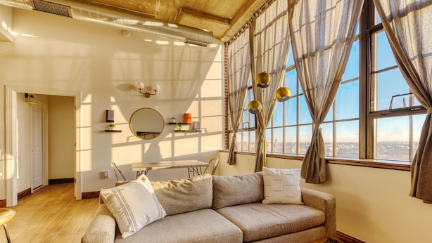 A living room with a beige sofa, a coffee table, and a large window with curtains. - Sosuite at Independence Lofts - Callowhill (Philadelphia)