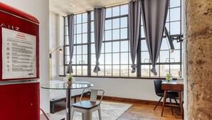 A hotel room with a glass table, a bed, a desk, and large windows with curtains. - Sosuite at Independence Lofts - Callowhill (Philadelphia)