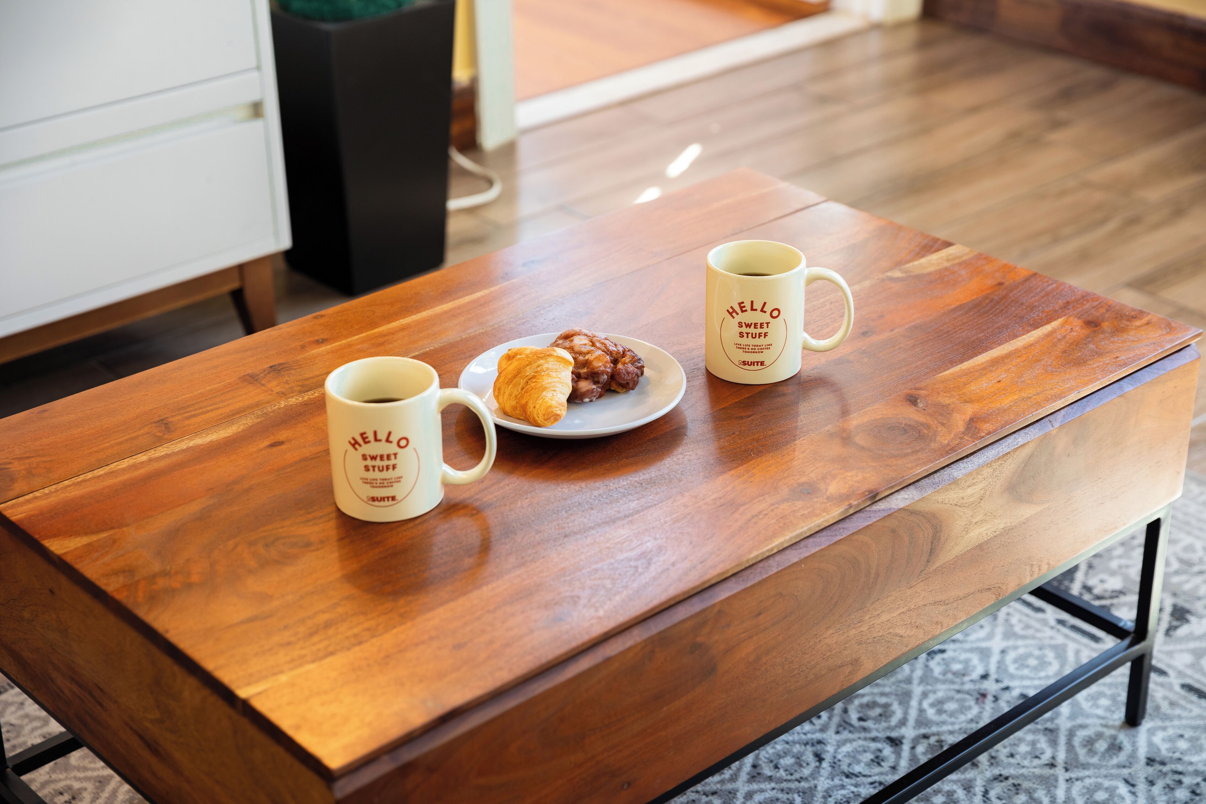 Een houten tafel met twee koffiemokken en een bord met eten.