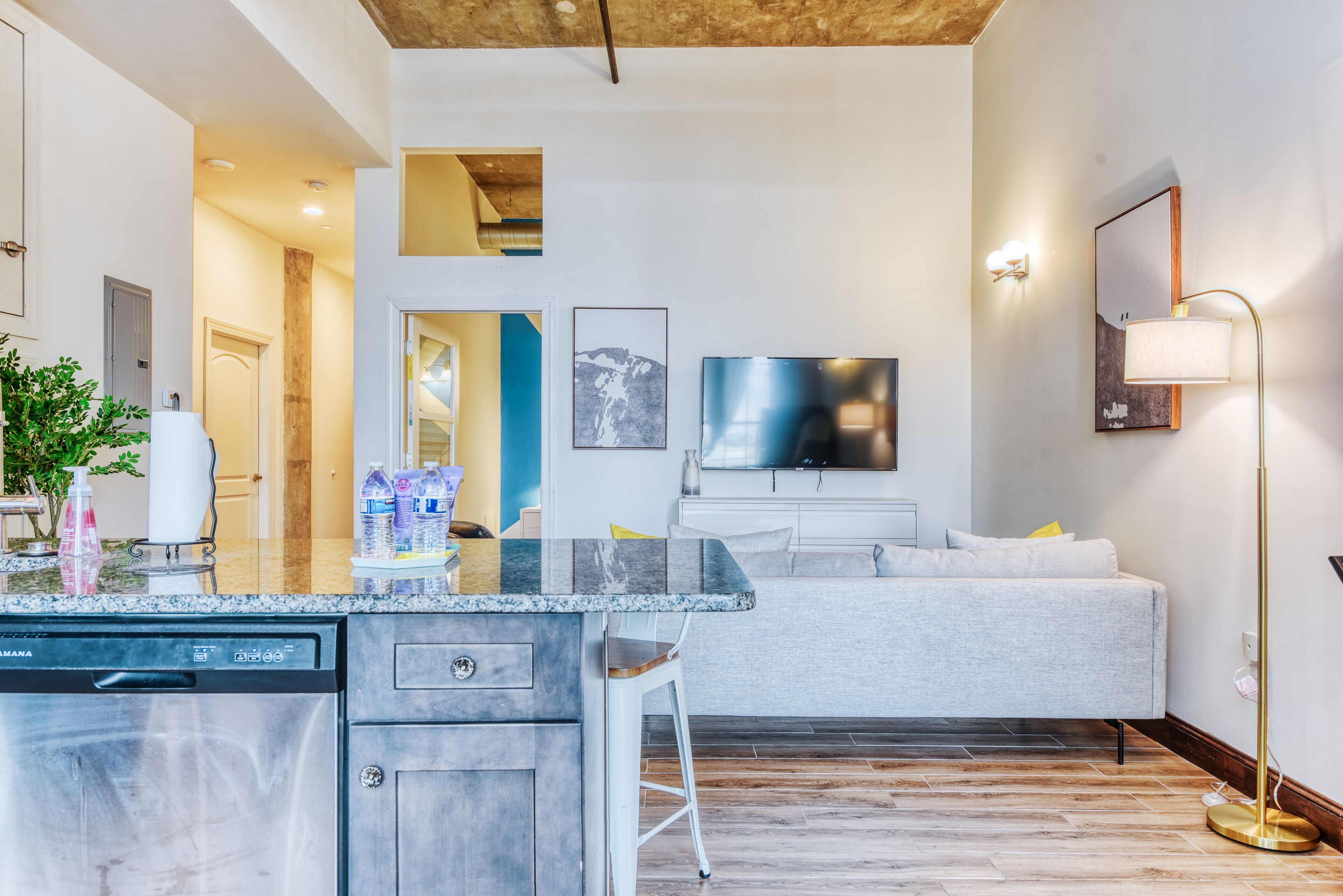 Eine moderne Küche mit Geschirrspüler, eine Bar mit Barhocker und ein graues Sofa im Wohnbereich.