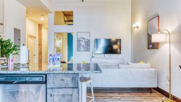 Eine moderne Küche mit Geschirrspüler, eine Bar mit Barhocker und ein graues Sofa im Wohnbereich.
