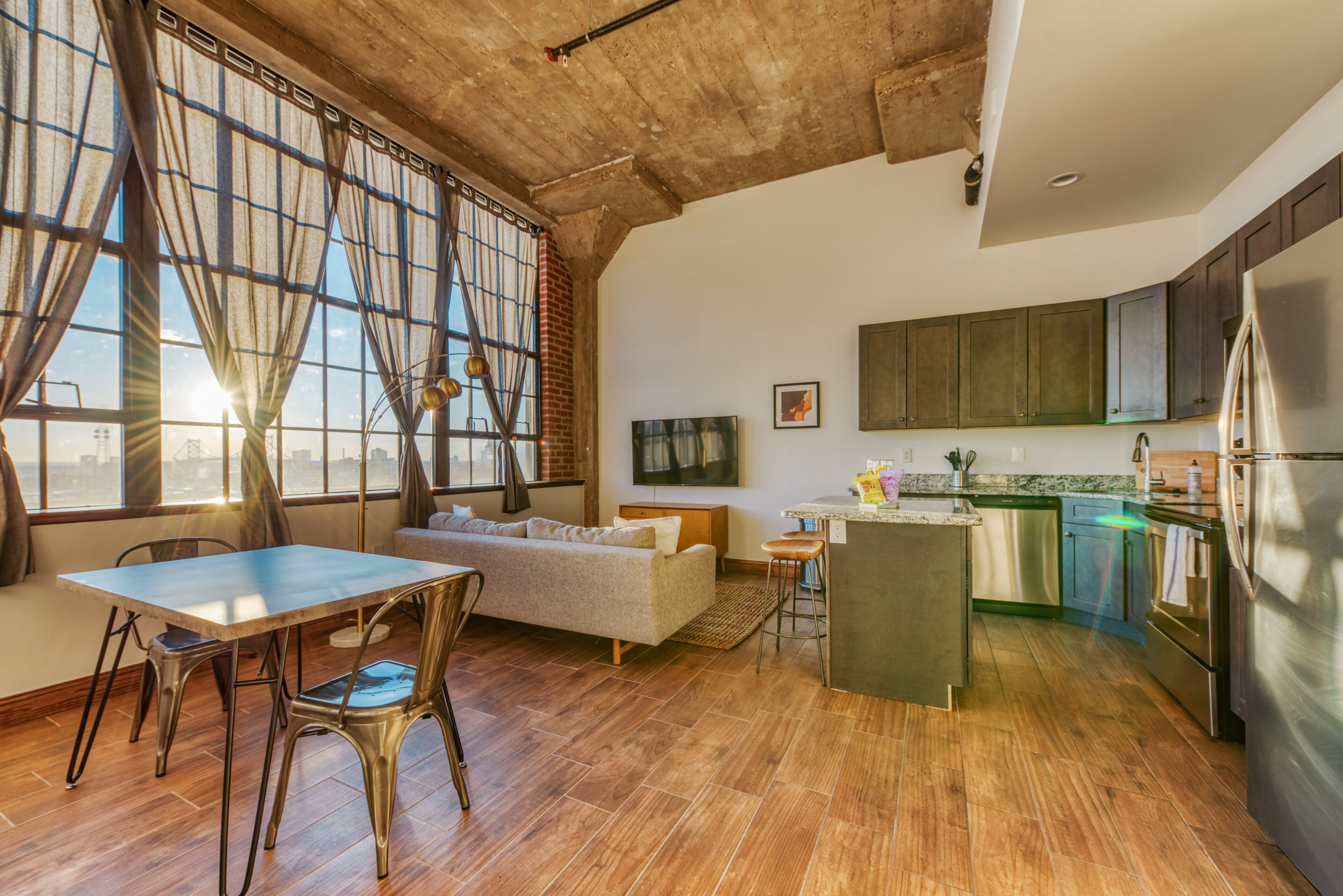 A spacious kitchen with wooden floors, a dining area with a table and chairs, and a large window with curtains.