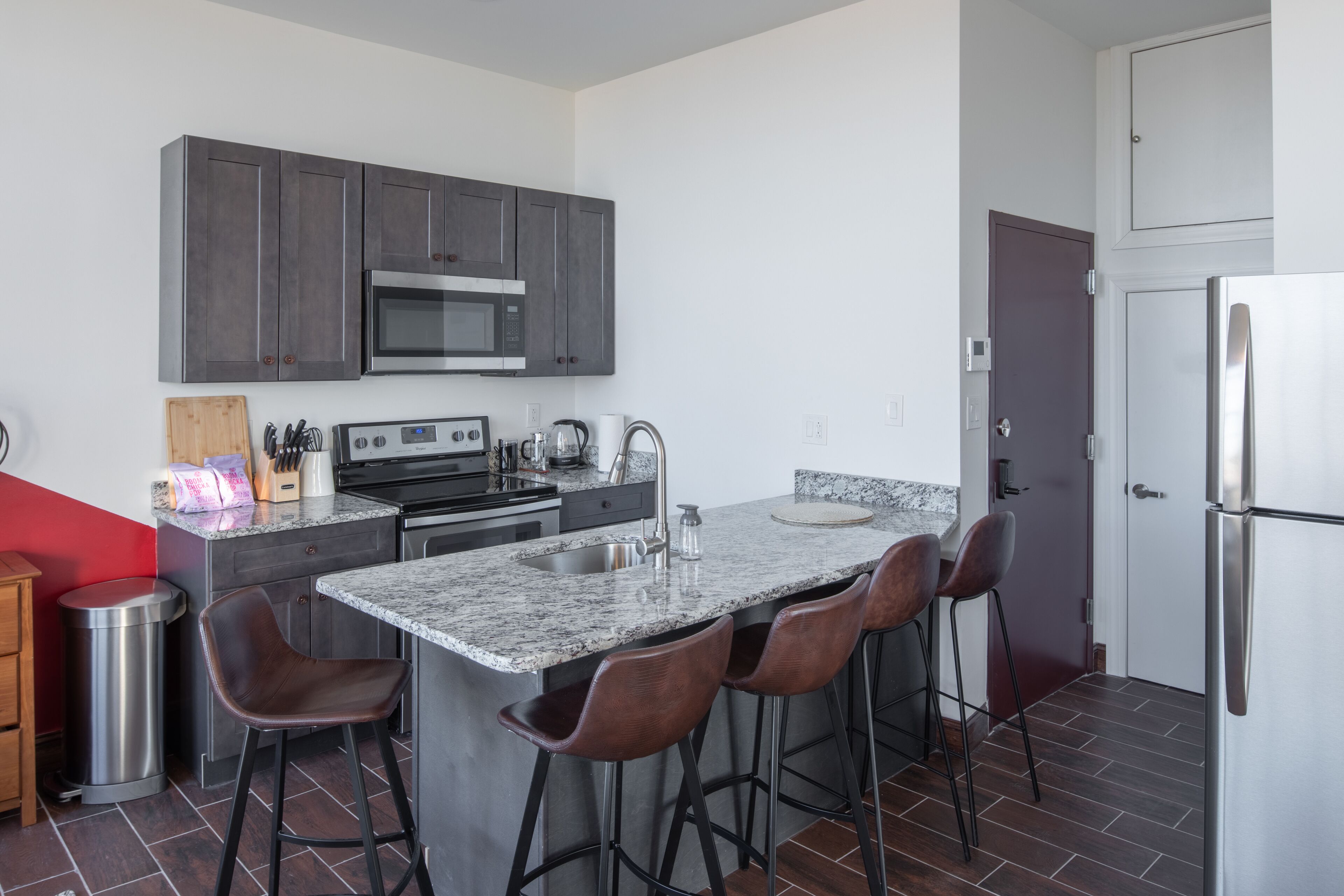 A modern kitchen with dark cabinets, stainless steel appliances, a granite countertop, and bar stools.