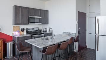 A modern kitchen with dark cabinets, stainless steel appliances, a granite countertop, and bar stools.