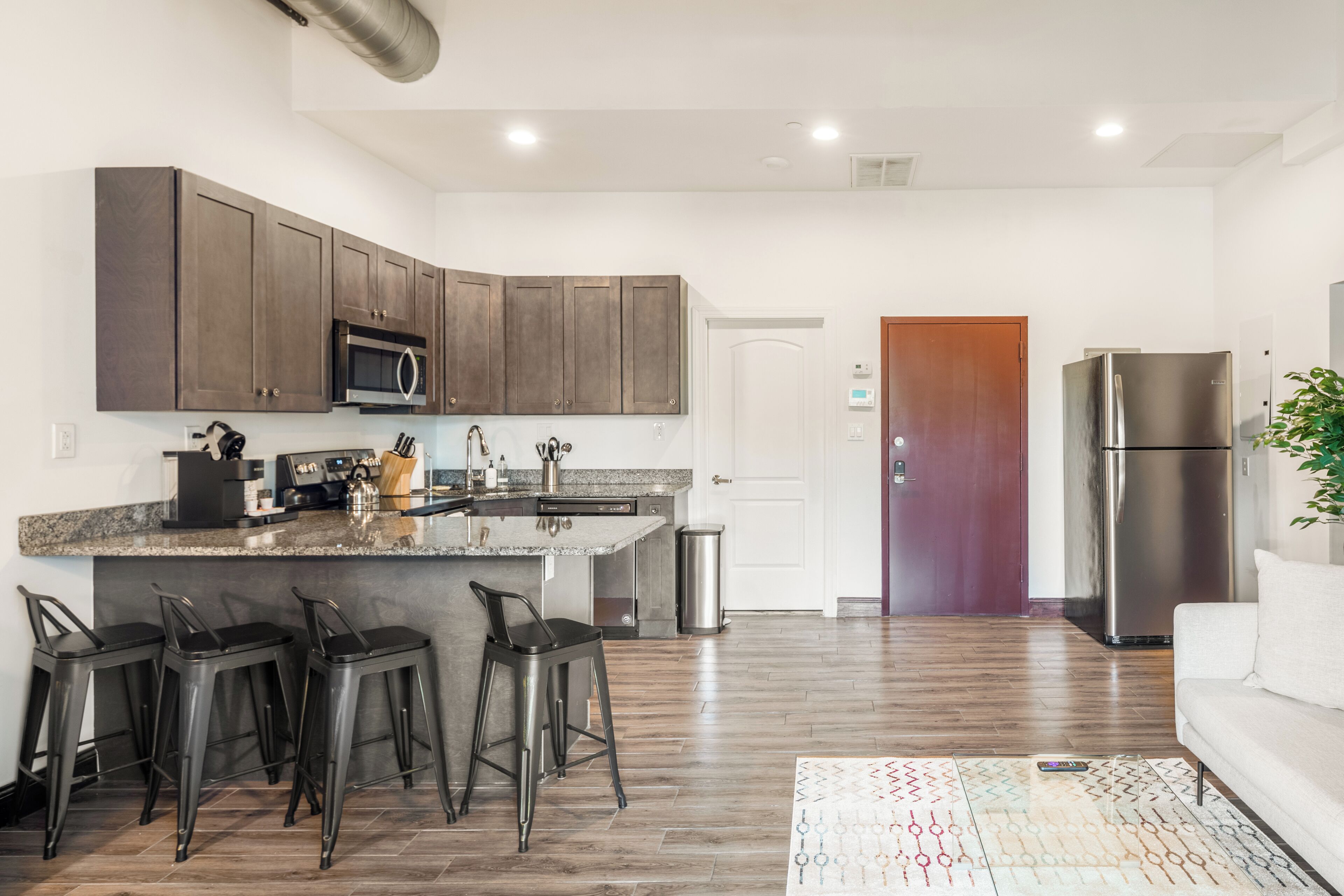 Una cocina moderna con armarios de madera oscura, un refrigerador de acero inoxidable y una zona de bar con taburetes.