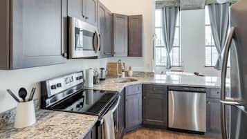 A modern kitchen with dark cabinets, stainless steel appliances, granite countertops, and a large window with curtains.