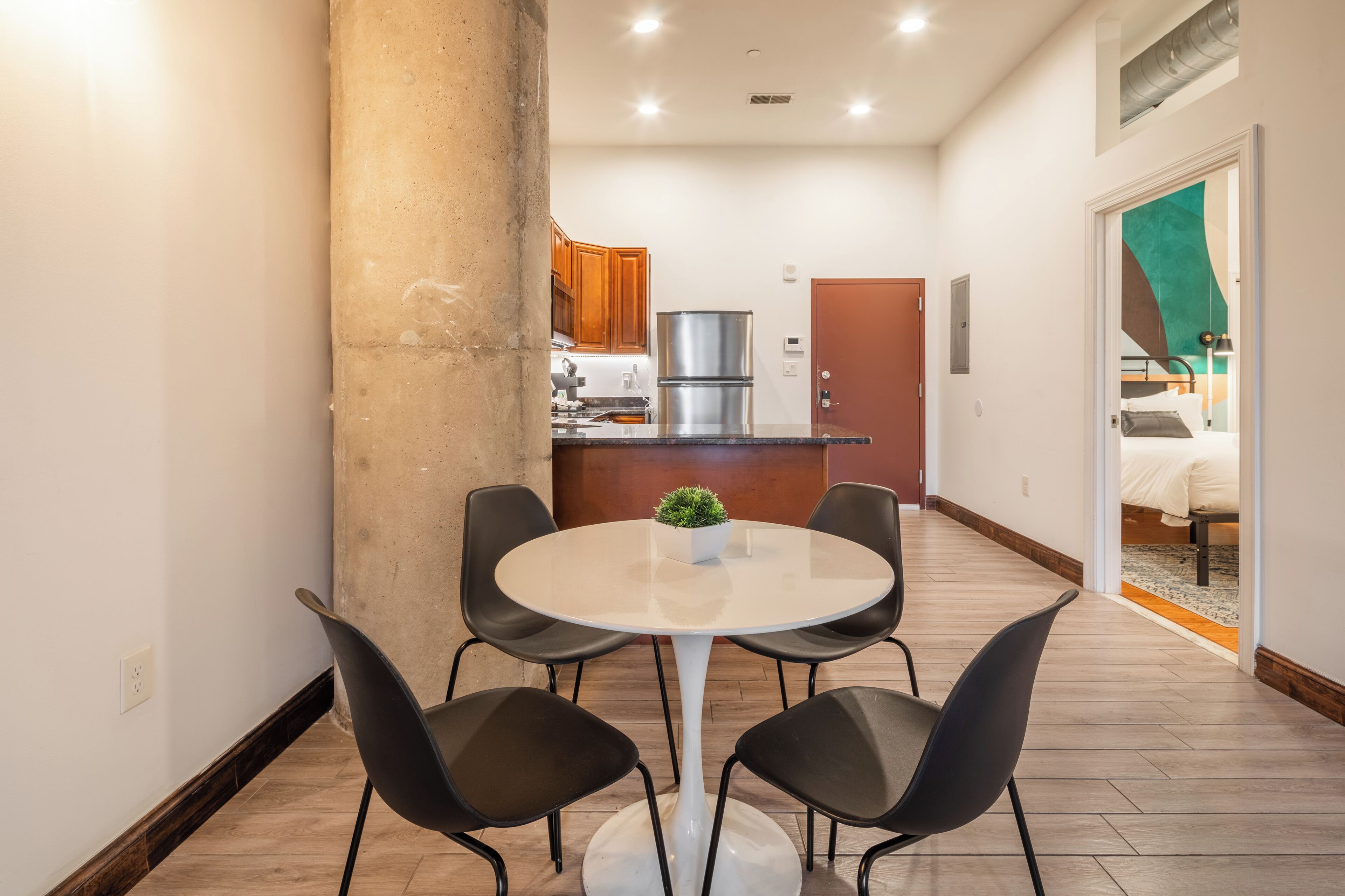 A modern kitchen with wooden cabinets, a stainless steel refrigerator, and a dining area with a white table and black chairs.