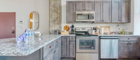 A modern kitchen with granite countertops, stainless steel appliances, and grey cabinetry.