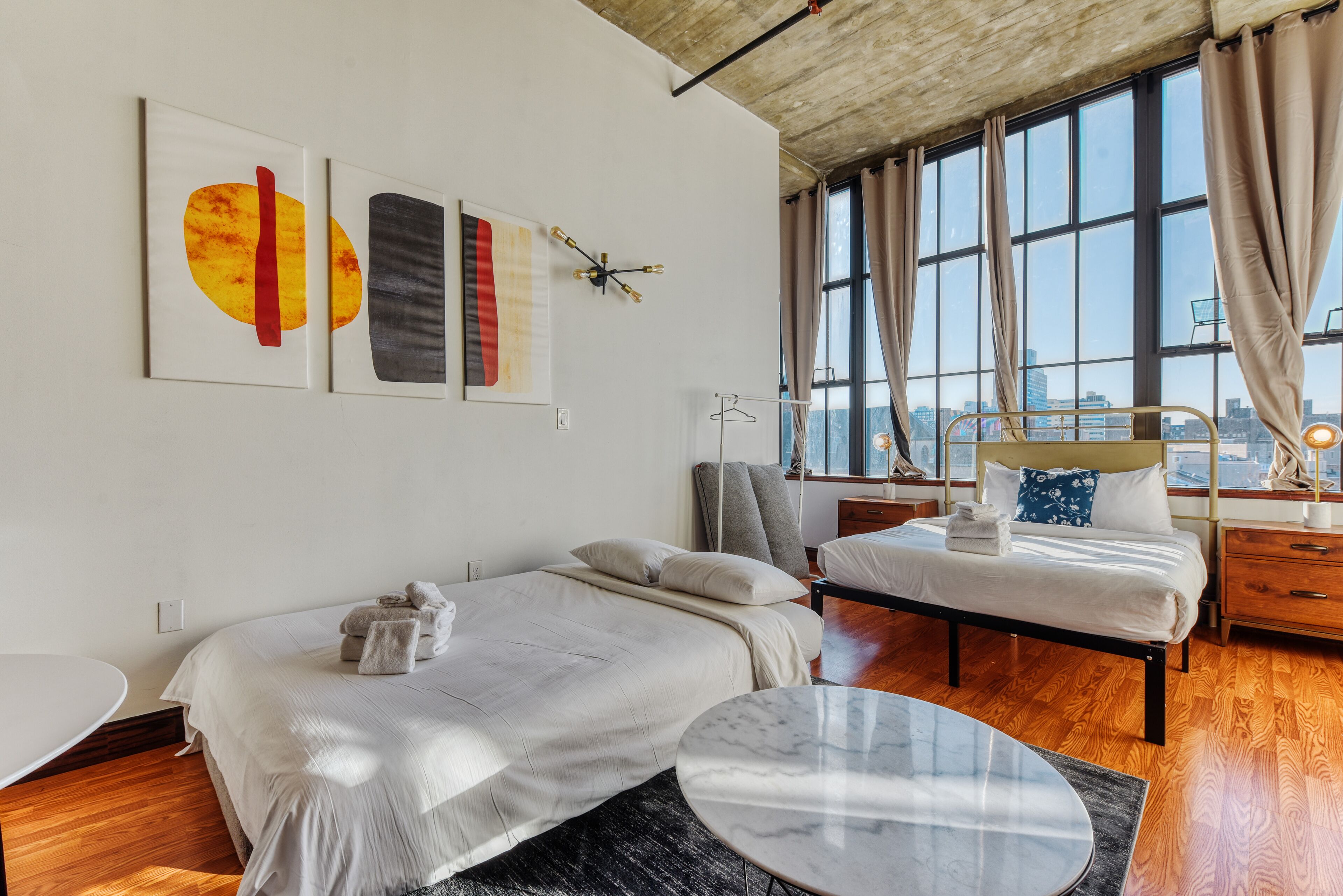 A modern bedroom with two beds, a marble table, and artwork on the wall.