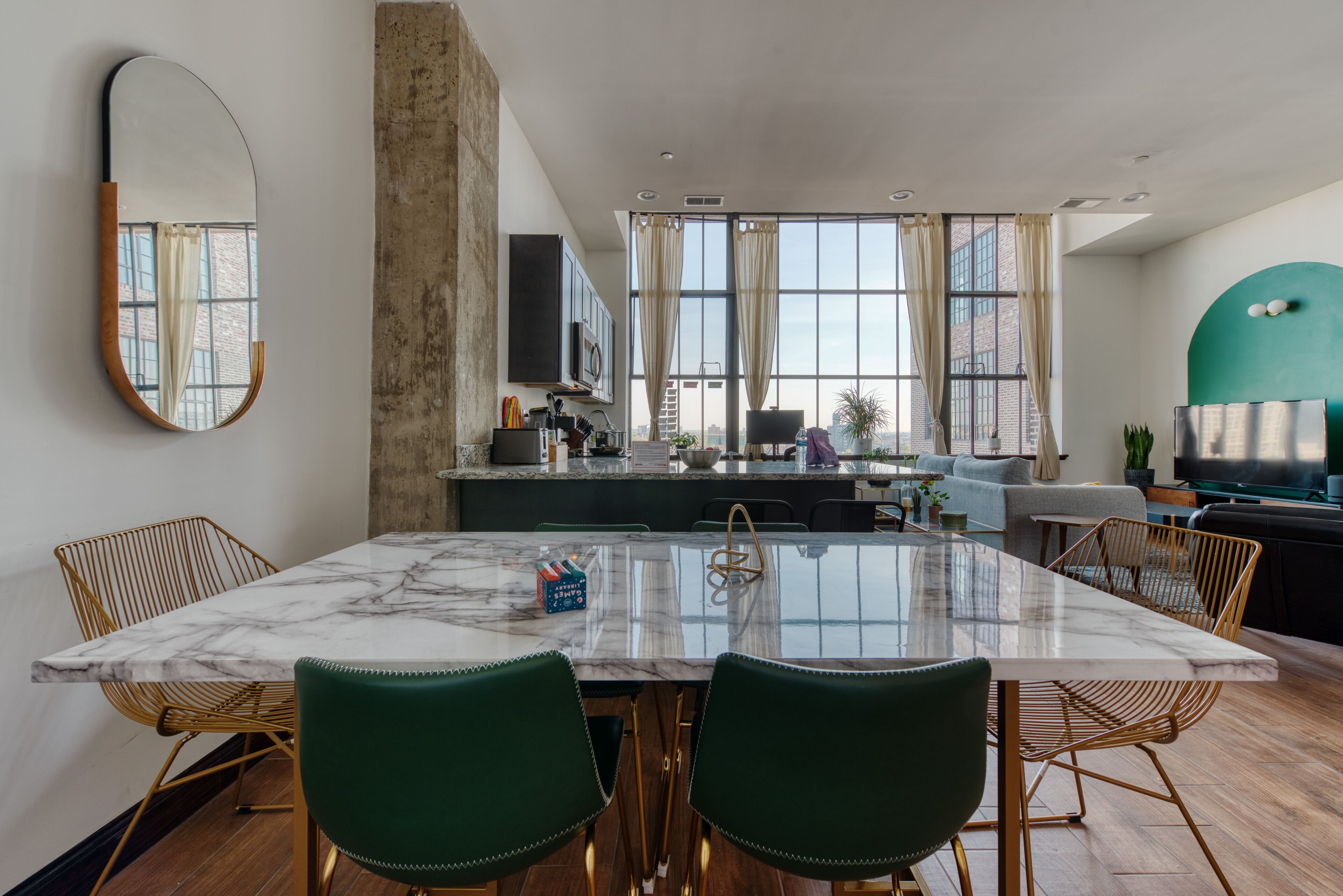 Een moderne keuken met een marmeren eiland, houten stoelen en een groot raam met gordijnen.