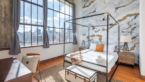A modern bedroom with a glass four-poster bed, a city view, and a marble-patterned wall. - Sosuite at Independence Lofts - Callowhill (Philadelphia)