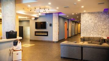 A lobby with a reception desk, a flat-screen TV, a fireplace, a sofa, and a wall with doodles.
