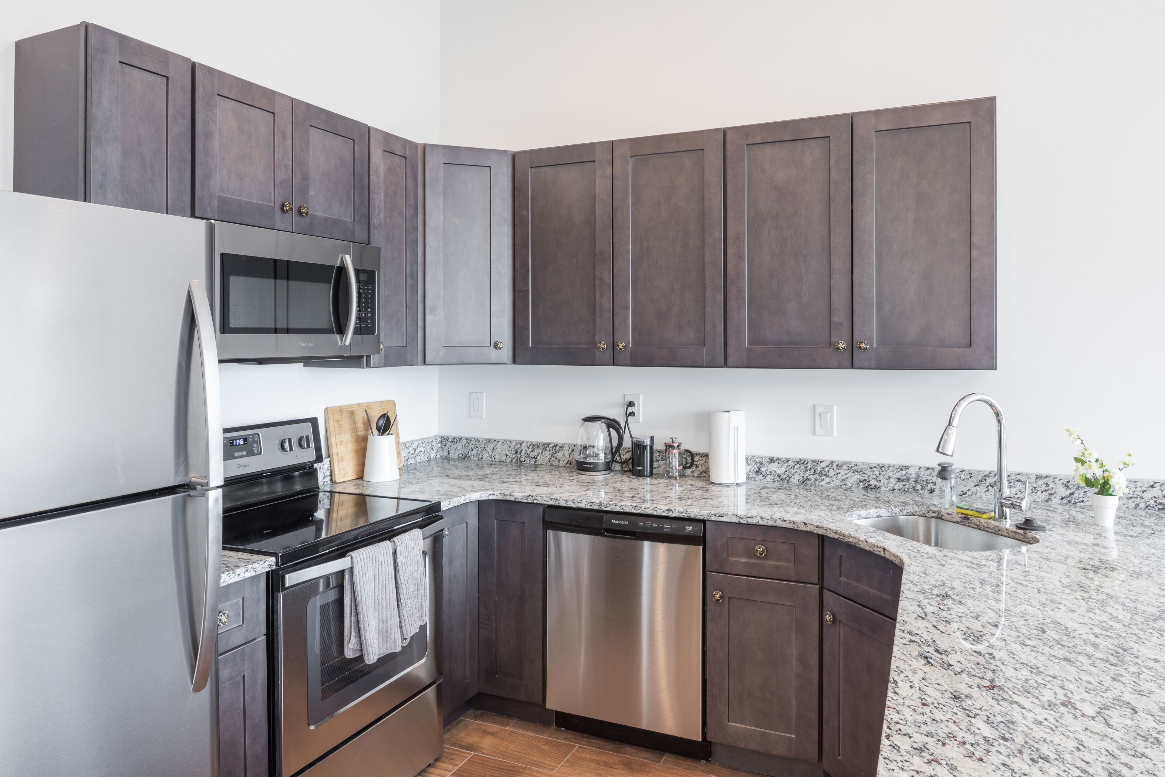 A modern kitchen with dark cabinets, stainless steel appliances, a granite countertop, and a built-in dishwasher.