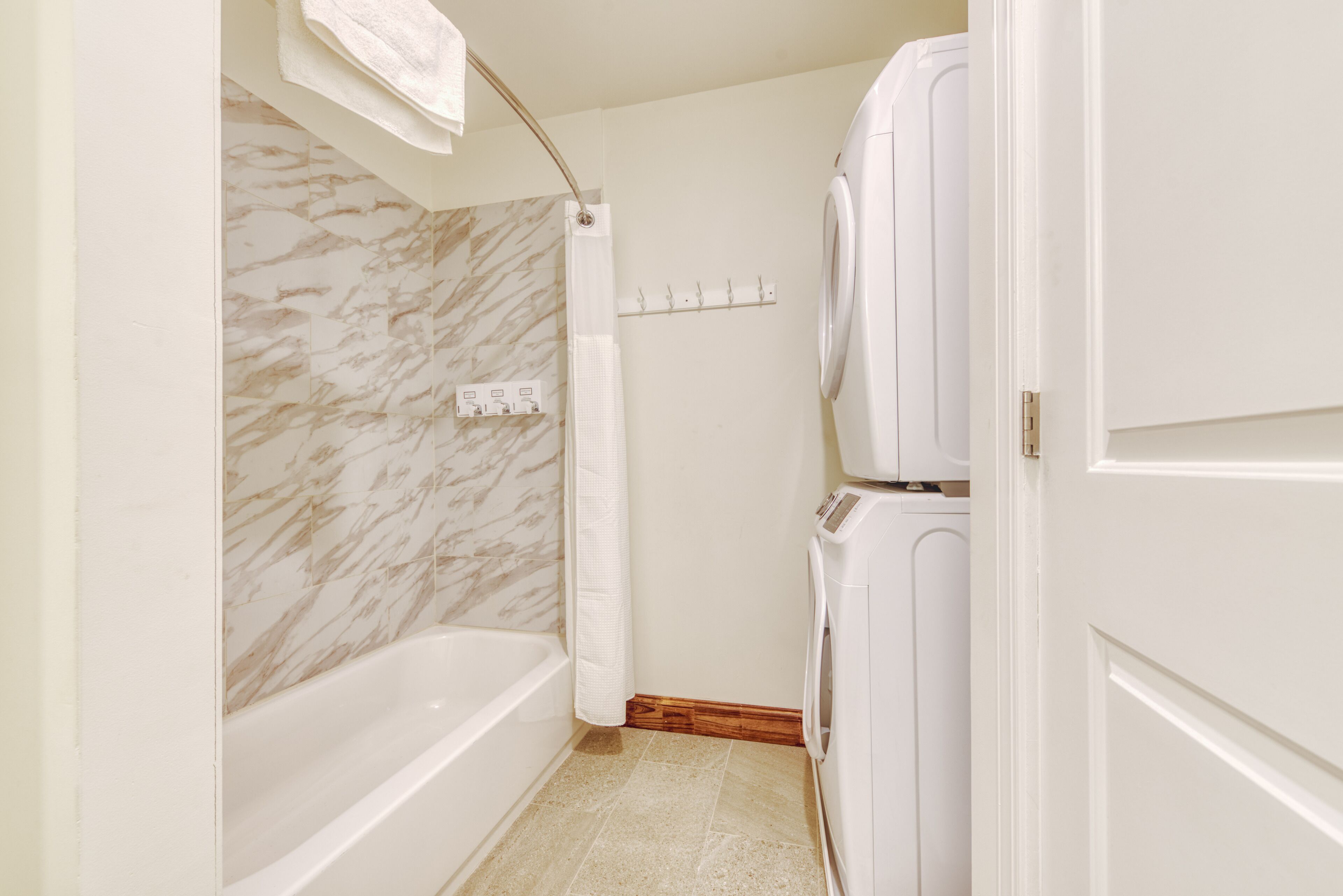 A bathroom with a marble wall, a bathtub, a washing machine, and a towel rack.