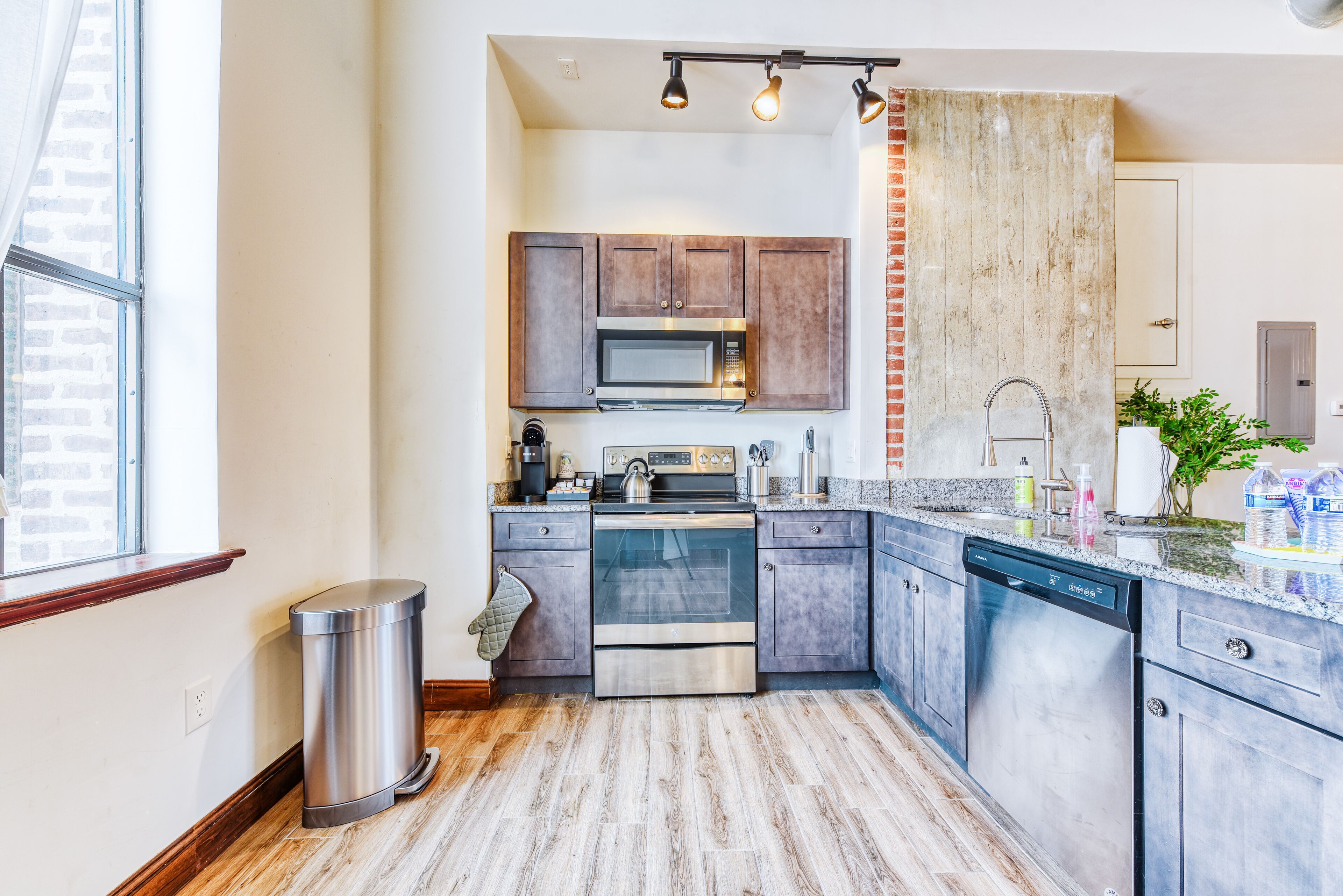 A compact kitchen with a stainless steel microwave, oven, and dishwasher, wooden cabinets, and a granite countertop.