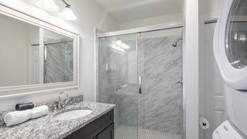 A bathroom with a marble sink, a glass shower enclosure, and a Samsung washing machine.