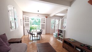 Un salon chaleureux avec un canapé, une table basse en bois, un coin repas avec une table et des chaises, et une bibliothèque.