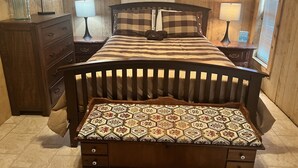 Une chambre à coucher avec un lit en bois, une table de chevet, une commode et une fenêtre avec des stores.