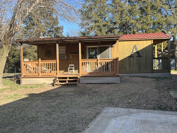 A wooden cabin with a porch, a deck, and a fenced yard.