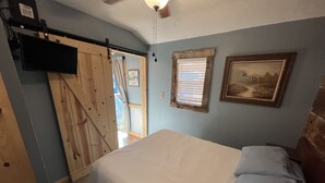 Ein Schlafzimmer mit einem Bett, einer Holztür, einem Fenster mit Jalousien und einem gerahmten Bild an der Wand.