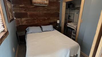 A bedroom with a wooden headboard, a ceiling fan, a bed with white bedding, a nightstand, and a mirror.