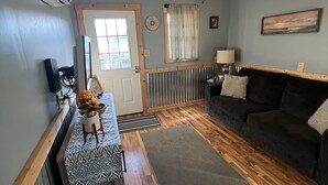 Ein Wohnzimmer mit Holzboden, Deckenventilator, Sofa, Couchtisch und einer Tür.