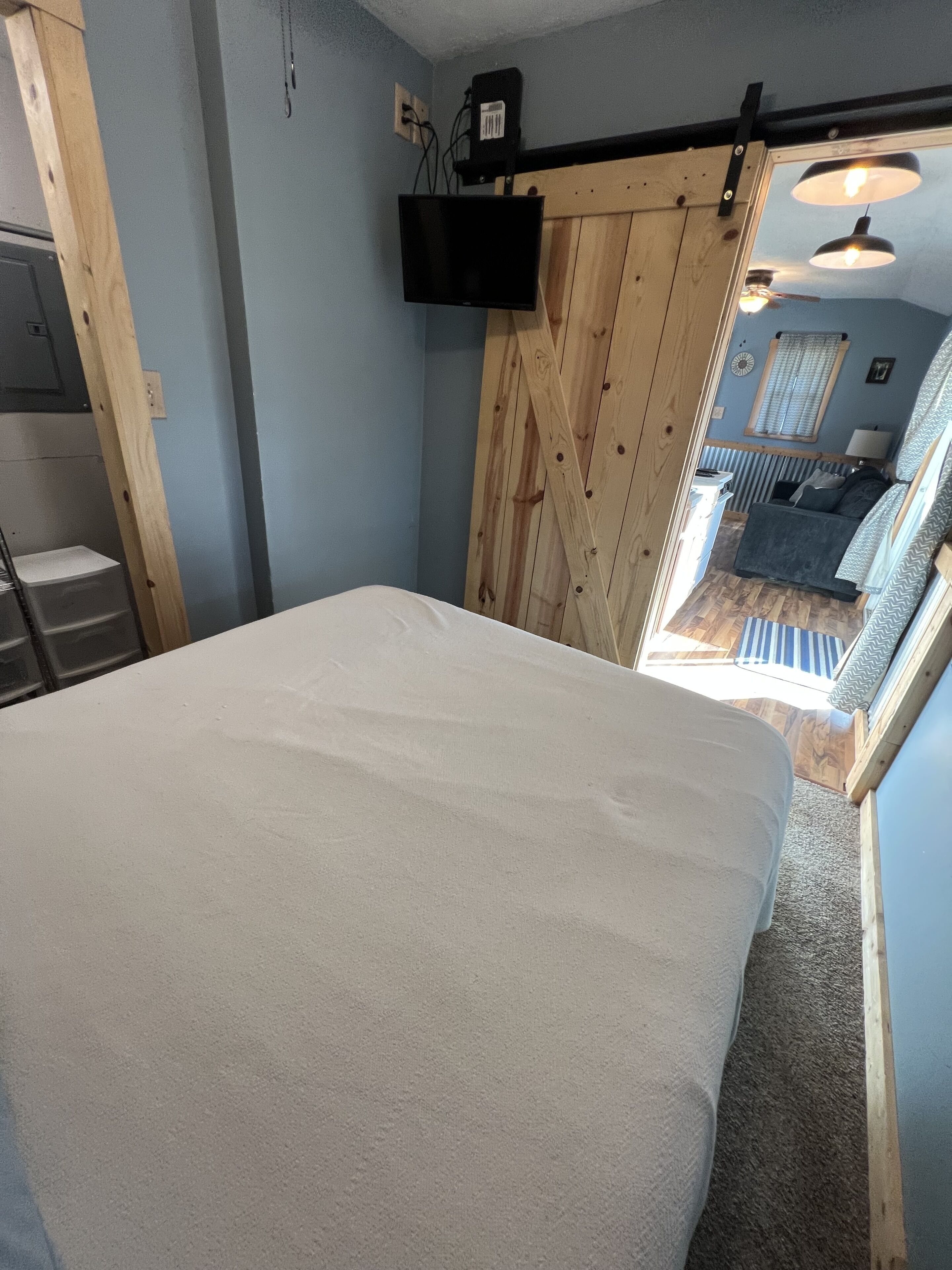 A bedroom with a bed, wooden walls, a TV mounted on the wall, and a view of a balcony with a railing.