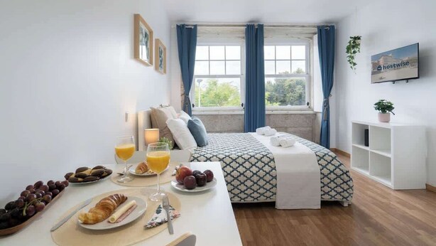 Une chambre d’hôtel moderne avec un lit soigneusement fait, une table à manger où le petit-déjeuner est servi, une télévision et une grande fenêtre avec des rideaux.