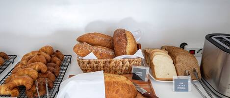 On trouve une variété de pains et de viennoiseries sur un comptoir, notamment des croissants, des baguettes et un pain estampillé « PAN DE CAMPO ».