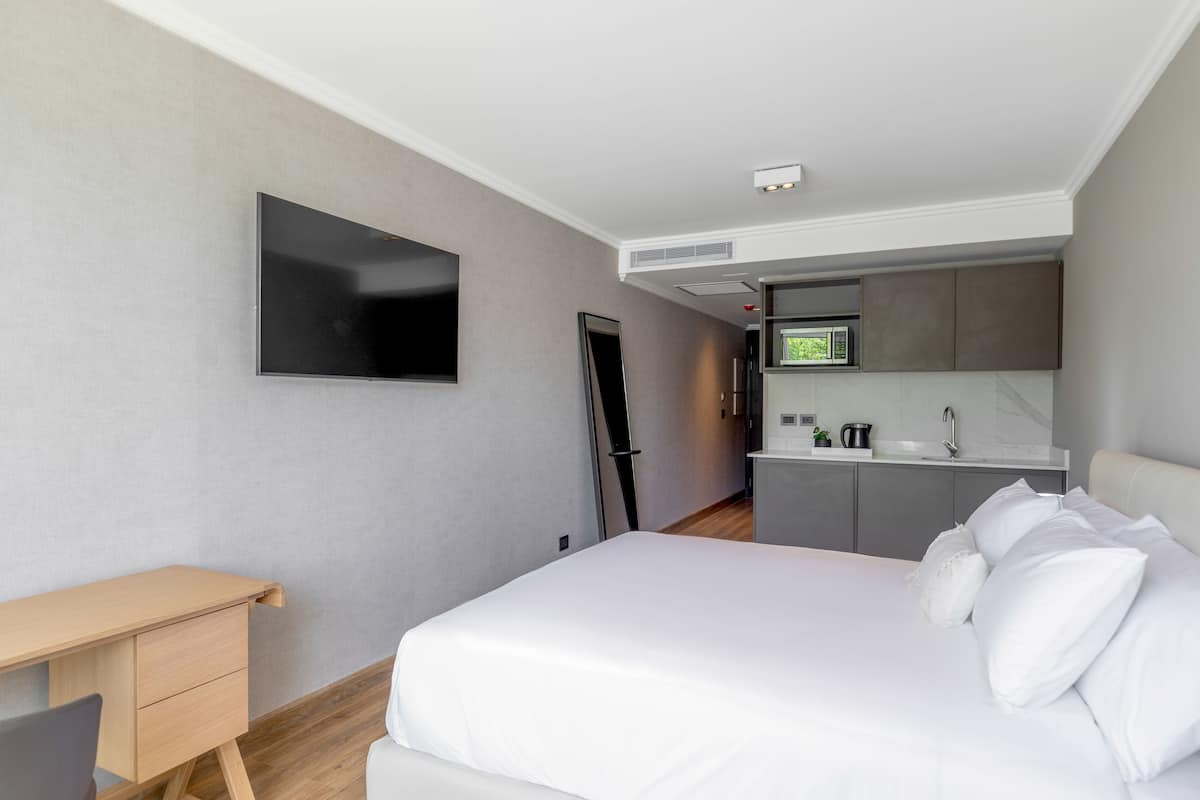 A modern hotel room with a bed, a desk, a flat-screen TV, and a kitchenette.