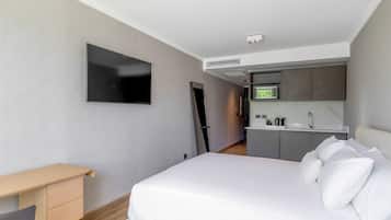 Una camera d'albergo moderna con un letto, una scrivania, una TV a schermo piatto e angolo cottura.