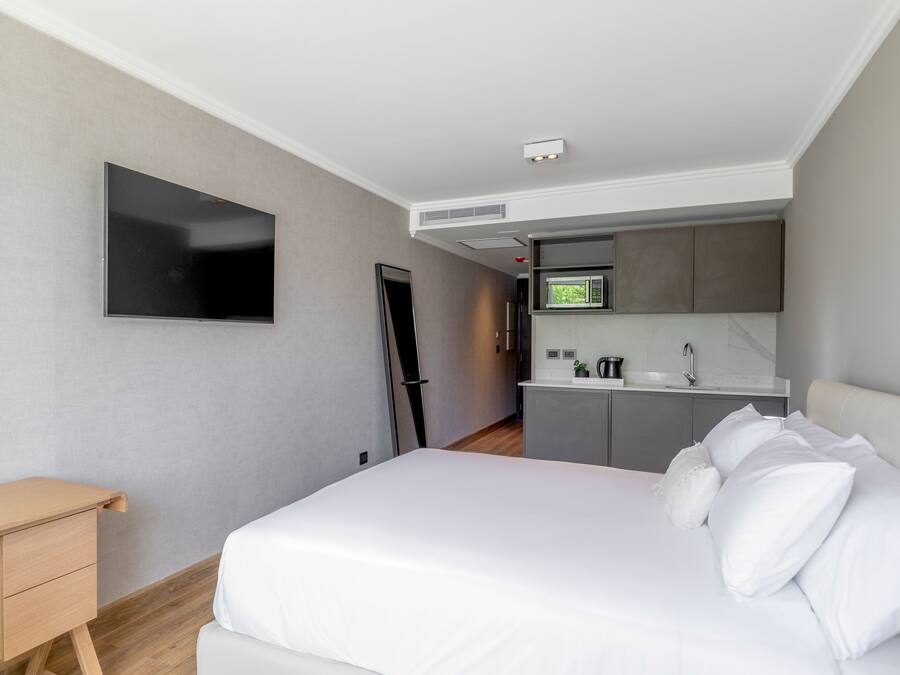Una camera d'albergo moderna con un letto, una scrivania, una TV a schermo piatto e angolo cottura.