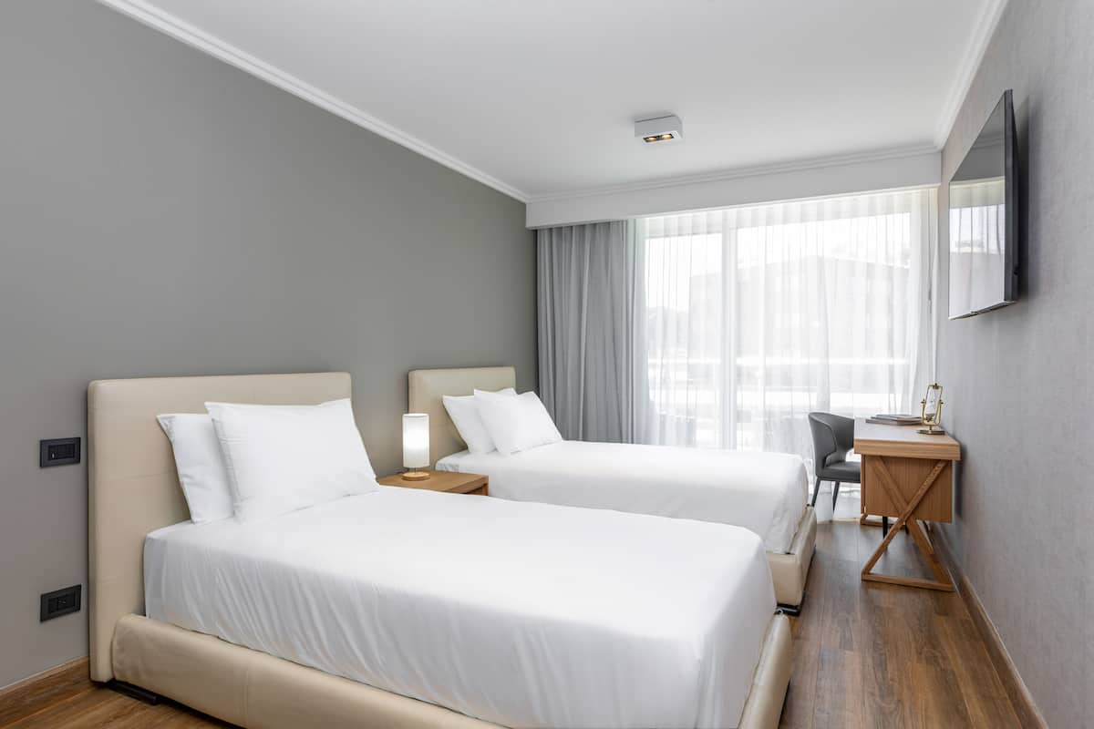 A hotel room with two beds, a desk, a chair, and a TV on the wall.