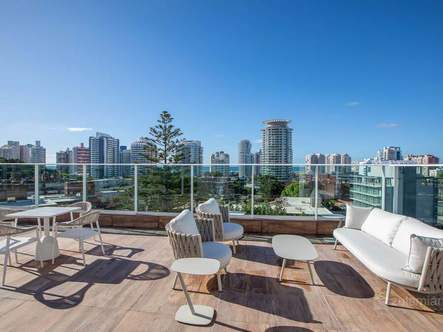 Una terraza en la azotea con vista al horizonte de la ciudad, equipada con un sofá, sillas y una mesa.