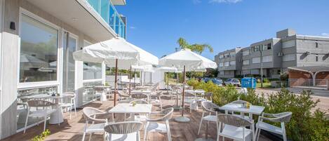 An outdoor patio with white tables and chairs, umbrellas, and a view of the street.