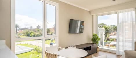 A modern living room with a large window, a flat-screen TV, a round table, and two sofas.