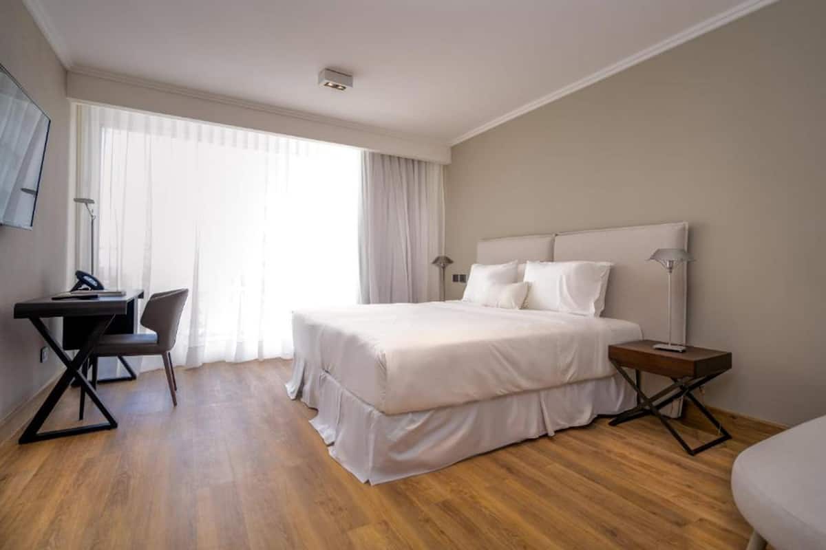 A modern hotel room with a large bed, a desk, and a chair.